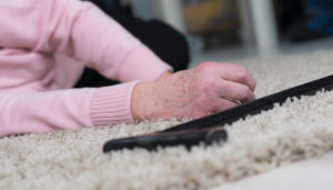 Close-up of an elderly woman's hand on a carpet, reaching for a fallen television remote. her sleeve is pink and detailed focus brings out the texture of the carpet.