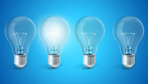Four light bulbs on a blue background, with the second from the left illuminated, symbolizing ideas or solutions.