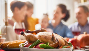 A family gathering around a dining table, focused on a roasted turkey centerpiece, with blurred faces in a warm, sunlit room, conveying a festive and joyful atmosphere.