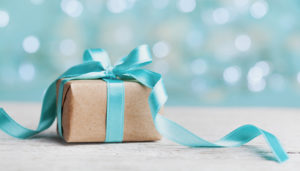 A small gift wrapped in brown paper tied with a delicate turquoise ribbon, set against a soft, blurred light blue background.