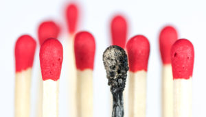 A row of red matchsticks with one charred matchstick standing out among the rest, against a white background.