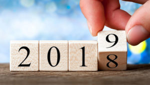 A hand changing the year from 2018 to 2019 using wooden blocks with numbers, set against a blurred background.