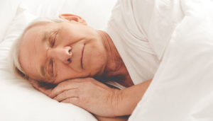Elderly man sleeping peacefully on a white pillow, with a serene expression and soft, warm lighting highlighting his features.