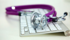 A purple stethoscope lies on a white computer keyboard, symbolizing the integration of healthcare and technology.