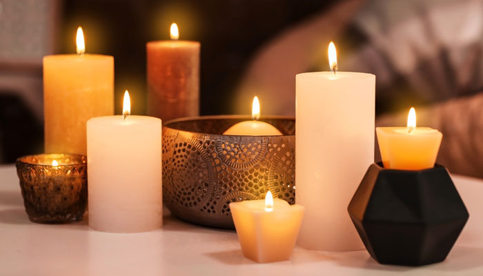 A collection of candles in various shapes and sizes, some in metal holders, glowing warmly on a table, creating a peaceful and serene ambiance.