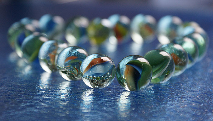 A circle of colorful glass marbles on a blue textured surface, reflecting light and showcasing a variety of swirling patterns in hues of blue, green, and brown.