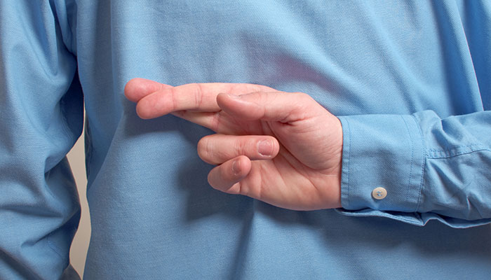 A person in a blue shirt with their fingers crossed behind their back, indicating secrecy or a hidden agenda.