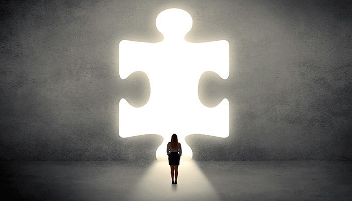 A woman stands facing a large, glowing puzzle piece-shaped opening in a wall, suggesting a concept of solution or opportunity.