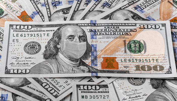 A u.s. hundred-dollar bill featuring benjamin franklin wearing a surgical mask, placed atop various other scattered hundred-dollar bills.