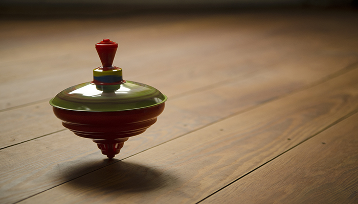 A colorful spinning top on a wooden floor, with soft lighting enhancing its red, green, and blue colors.